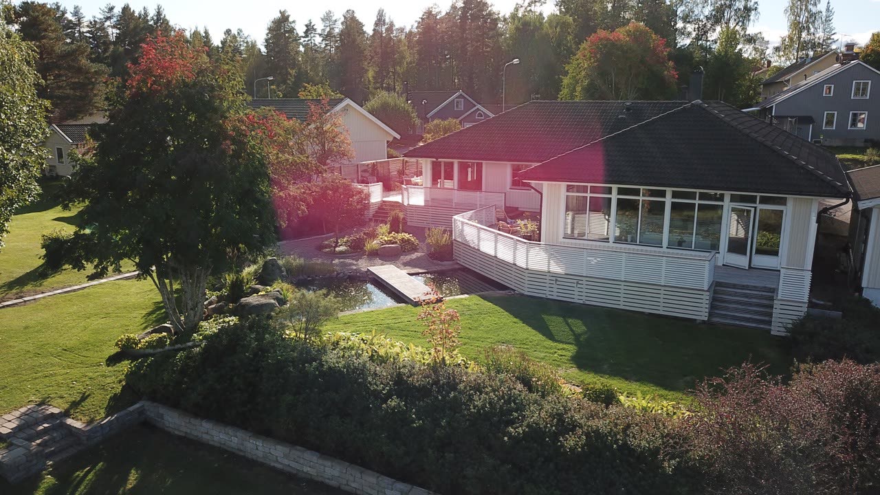Vit villa med spjälinklädda trädäck, spegeldamm med träspång och klippta gräsytor en solig höstdag